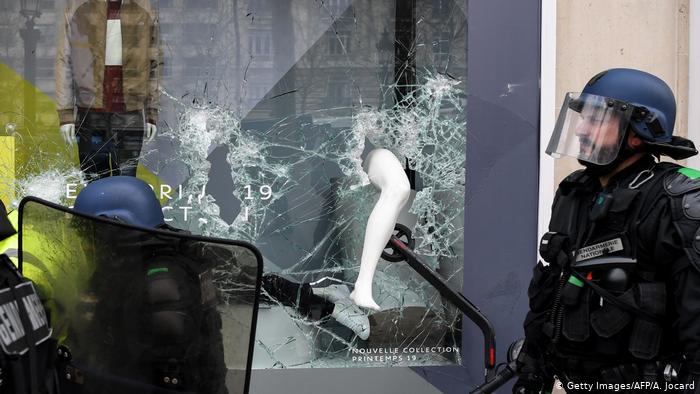La police anti-émeute française passe devant un scooter vu dans une vitrine brisée
